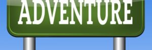 Green road sign with the word "ADVENTURE" in bold white letters against a blue sky background.