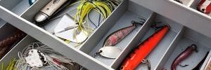 Open tackle box with assorted fishing lures, hooks, fishing line, and bobbers organized in compartments.
