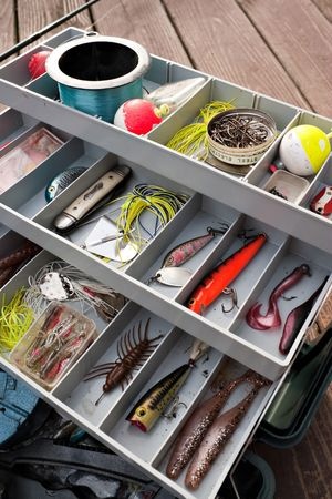 Open tackle box with assorted fishing lures, hooks, fishing line, and bobbers organized in compartments.