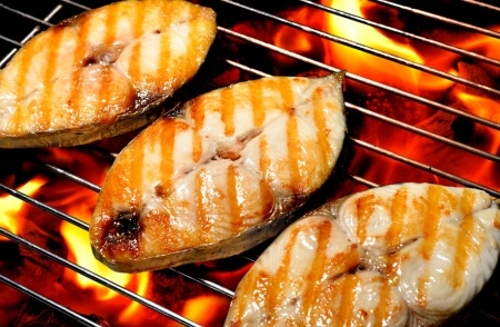 Three pieces of fish with grill marks cooking over an open flame on a metal grill.