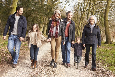 Six people, including two children, walk together on a wooded path during daytime, dressed in casual winter clothing.