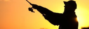 Silhouette of a person fishing with a rod at sunset, with an orange sky in the background.