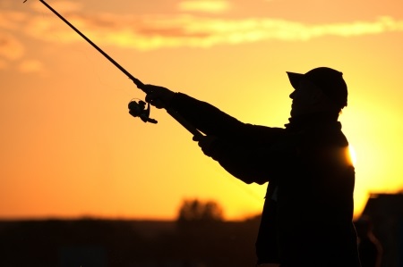 Silhouette of a person fishing with a rod at sunset, with an orange sky in the background.