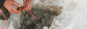 A person’s hands tying fishing line near a hole in the ice while ice fishing.