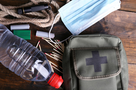 Survival kit items on a wooden surface: face mask, water bottle, rope, matches, lighter, and first aid pouch.