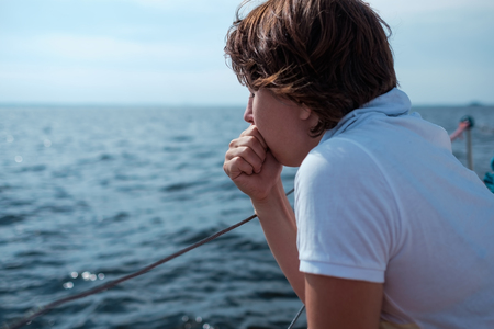 A person in a white shirt leans on a railing and looks thoughtfully at the water on a boat.