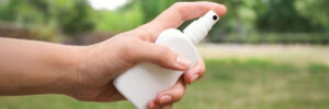 A hand holding and spraying a white plastic bottle, with a grassy outdoor background.