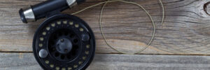 A close-up of a fishing rod and reel with fishing line, resting on a weathered wooden surface.