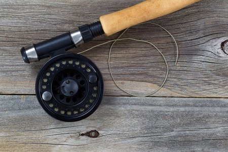 A close-up of a fishing rod and reel with fishing line, resting on a weathered wooden surface.