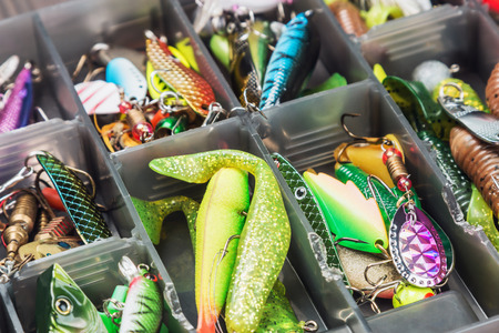 A tackle box filled with assorted colorful fishing lures and bait, organized in separate compartments.