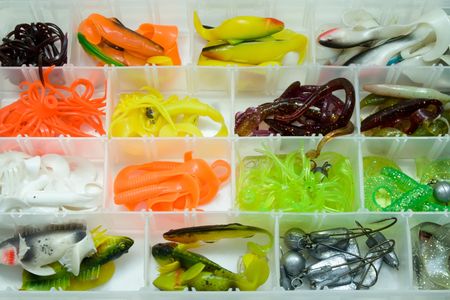 A tackle box with assorted plastic fishing lures and soft baits organized by color and shape in compartments.