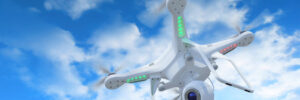 A white quadcopter drone with a camera flies against a blue sky with scattered clouds.