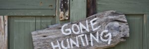 A weathered wooden sign reading "Gone Hunting" hangs on a green, rustic door with visible handles.