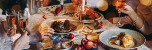 A group of people sits at a festive table with candles, plates of food, and glasses of champagne.