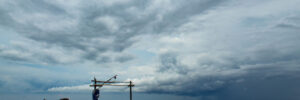 A small wooden boat floats on calm sea under a cloudy, overcast sky with dark storm clouds in the distance.