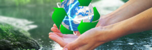 Hands holding a digital globe with a green recycling symbol above a body of water, symbolizing environmental conservation.