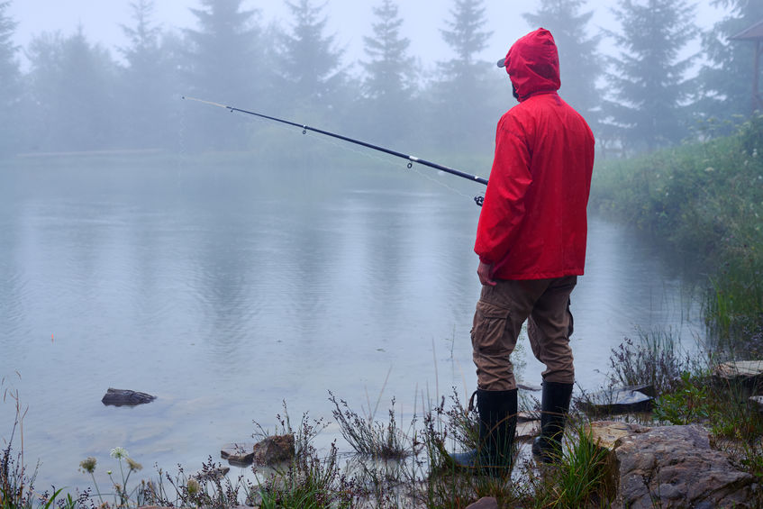 Side view of man in waterproof jacket fishing on Lake