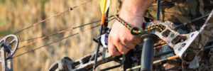 Person in camouflage holding a compound bow and loading an arrow outdoors in a field.