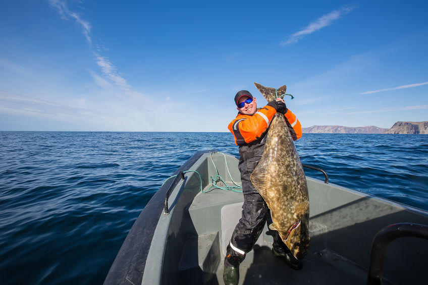 Man holding up big fish on a boat in the middle of the water