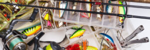 Tackle box with various fishing lures, reels, rods, line, and fishing tools arranged on a white surface.