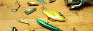 Fishing rods, a reel, and various fishing lures and spoons are arranged on a wooden surface.