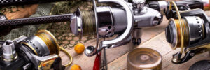 Fishing reels, rods, line, bait balls, and tackle gear arranged on a wooden surface, with a fishing net in the background.