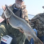 Person holding a large fish on a boat, wearing a blue cap and camouflage jacket, with another person beside them.