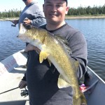 Person holding a fish in a boat on a lake, with another person in the background also fishing.