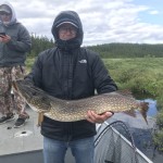 Person holding a large fish while standing on a boat, with another person in the background under a cloudy sky.