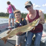 Adult and child holding large fish on a boat. Another child in the background looks towards the water under a clear sky.
