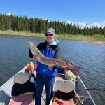 Person on a boat holding a large fish with trees and water in the background.