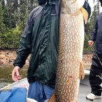 Person in raincoat holding a large fish on a boat with trees in the background.