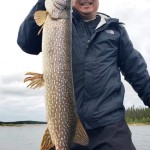 Man holding a large fish on a boat with overcast sky in the background, while smiling at the camera.