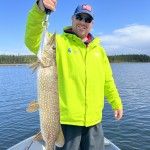 Person in bright green jacket holding a large fish on a boat in a lake under a clear blue sky.